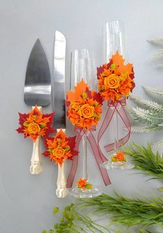 orange flowers are placed in wine glasses with silverware and greenery next to them