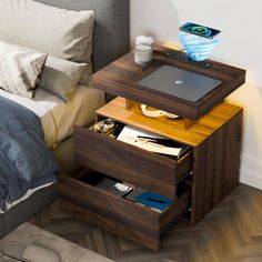 a laptop computer sitting on top of a wooden table next to a bed with pillows