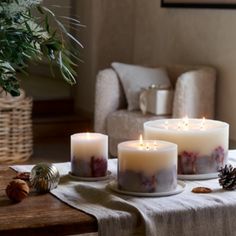 three lit candles sitting on top of a table next to a vase and pine cones