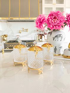 three vases with pink flowers in them on a white countertop next to gold accents