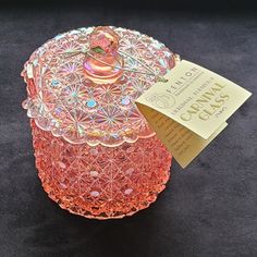 a pink glass jar sitting on top of a black table next to a yellow tag