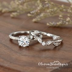 two wedding rings with leaves on them sitting on a wooden table next to flowers and greenery