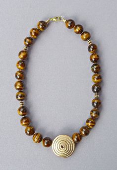 A very special and elegant piece of jewelry from my studio: A perfectly and elaborately hand-forged and structured large golden spiral of over 30 mm diameter on a closed medallion is the eye-catcher and the centerpiece of this truly unusual and exquisite necklace. The vividly banded golden-brown beads from tiger's eye have diameters of approx. 15 mm and are separated from each other by small gold beads and symmetrically placed gold rondelles. The necklace ends are decorated and protected with go Elegant Bronze Spiral Jewelry, Big Tiger, Golden Spiral, Stainless Steel Wire, Tiger's Eye, Golden Brown, Jewelry Tutorials, Hand Forged, Gold Beads