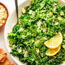 a salad with lemons, almonds and greens in a bowl next to crackers