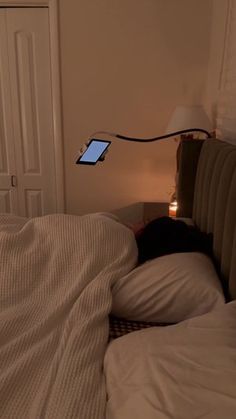 a bed with white sheets and a cell phone on the headboard next to it