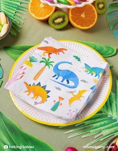 a paper plate with dinosaurs on it next to some oranges and kiwi slices