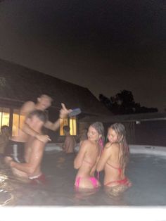 three people in a hot tub at night with one person pointing to the side and two others holding something