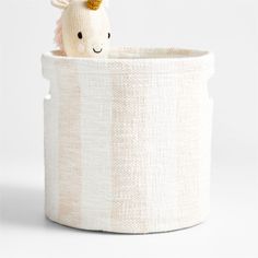 a stuffed animal sitting inside of a white fabric storage container with stripes on it's sides