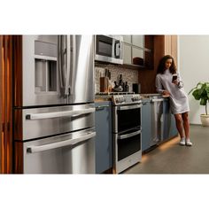 a woman in a kitchen looking at her cell phone while standing next to an oven