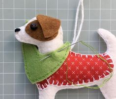 a dog ornament with a red sweater and green vest hanging on a wall