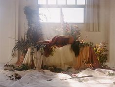 a woman laying on top of a bed covered in blankets and flowers next to a window