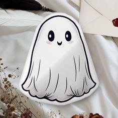 a white ghost pillow sitting on top of a bed next to an envelope and flowers