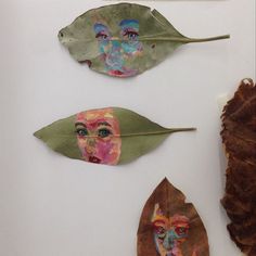 three leaf shaped artwork pieces with faces on them