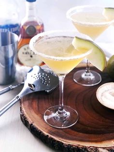 two martinis sitting on top of a wooden tray next to an avocado