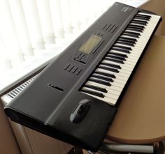 an electronic keyboard sitting on top of a wooden table next to a window with blinds