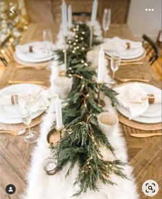 the table is set with white plates and silverware, gold candlesticks and greenery