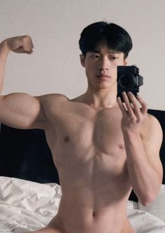 a shirtless man taking a selfie with his camera in front of him on the bed