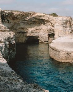 a body of water near a rocky cliff with a cave in the middle and blue water below