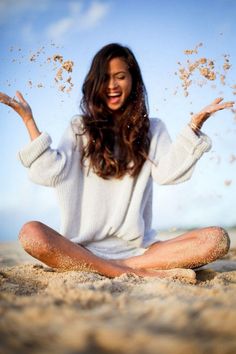 a woman sitting in the sand with her hands out and food flying up into the air