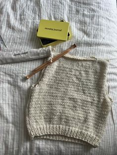 a sweater and pencils on a bed with an empty box next to the blanket