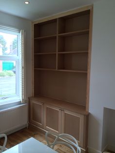 an empty living room with wooden shelves and white chairs in front of a large window