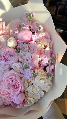 a bouquet of pink and white flowers sitting on top of a paper wrapper in someone's hand