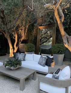 an outdoor living area with couches, tables and potted trees in the background