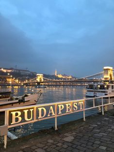 there is a sign that says budapest next to the water with boats docked in it