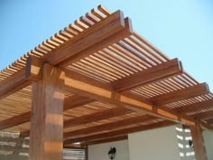 a wooden pergolated structure in front of a white wall and light blue sky