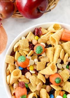 a bowl filled with candy cornflakes next to an apple and some other fruit