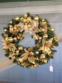 a christmas wreath hanging on the side of a door with gold ornaments and bows around it