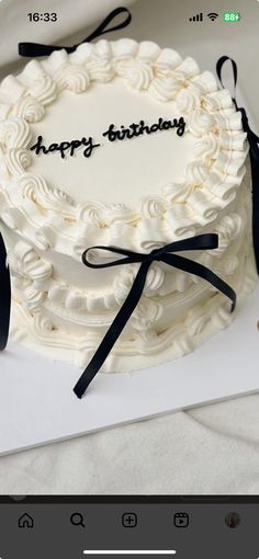 a white cake with black ribbon and happy birthday written on the top is sitting on a table