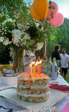 a birthday cake sitting on top of a table covered in flowers and balloons with lit candles