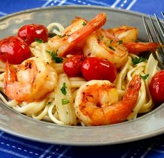 a plate of shrimp and tomato pasta on a blue table cloth with a fork in it