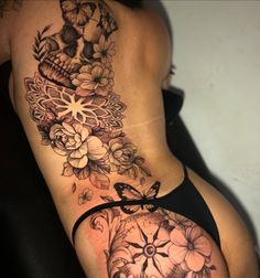 a woman's stomach with flowers and a skull tattoo on her side ribcage