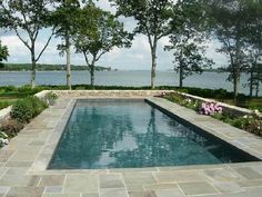 an outdoor swimming pool surrounded by trees and flowers next to the water's edge