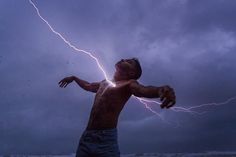 a man standing on top of a beach under a cloudy sky holding a lightning bolt