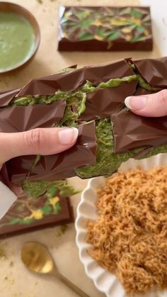 a person is holding a chocolate bar with green toppings on it and some rice in the background