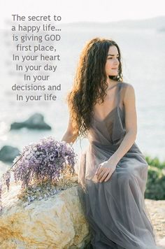 a woman sitting on top of a rock next to the ocean with flowers in her hand