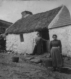 two women standing in front of a thatched house