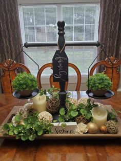 a wooden tray with candles and plants on it in front of a window, next to a sign that says welcome