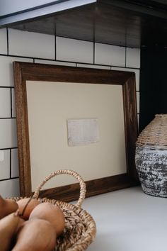 a basket sitting on top of a white counter next to a framed photo and vase