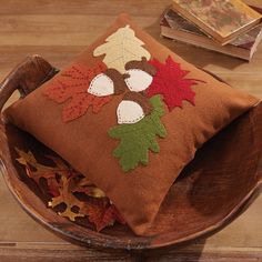 a wooden bowl with a decorative pillow on top of it and some leaves in the middle