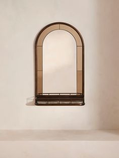 an arched window on the side of a white wall next to a shelf with a mirror