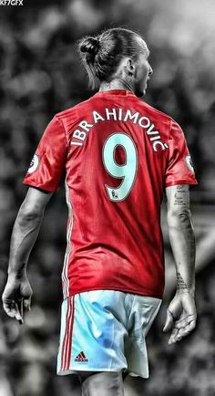 a man in a red shirt and blue shorts standing on a soccer field with his back to the camera