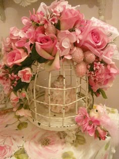 a white birdcage filled with pink flowers on top of a floral covered table