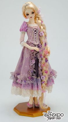 a doll with long blonde hair wearing a purple dress and holding a pink flower in her hand