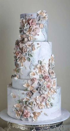 a three tiered wedding cake with flowers on the top and bottom, sitting on a silver platter