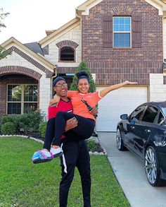 two people standing in front of a house with their arms around each other and one person holding an infant