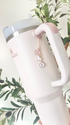 a person holding a white coffee cup with a chain attached to the handle and flower charm on it